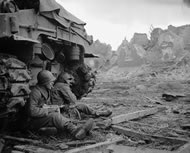 Two US infantrymen sneaking a smoke behind a tank in Geich, Germany, December 1944